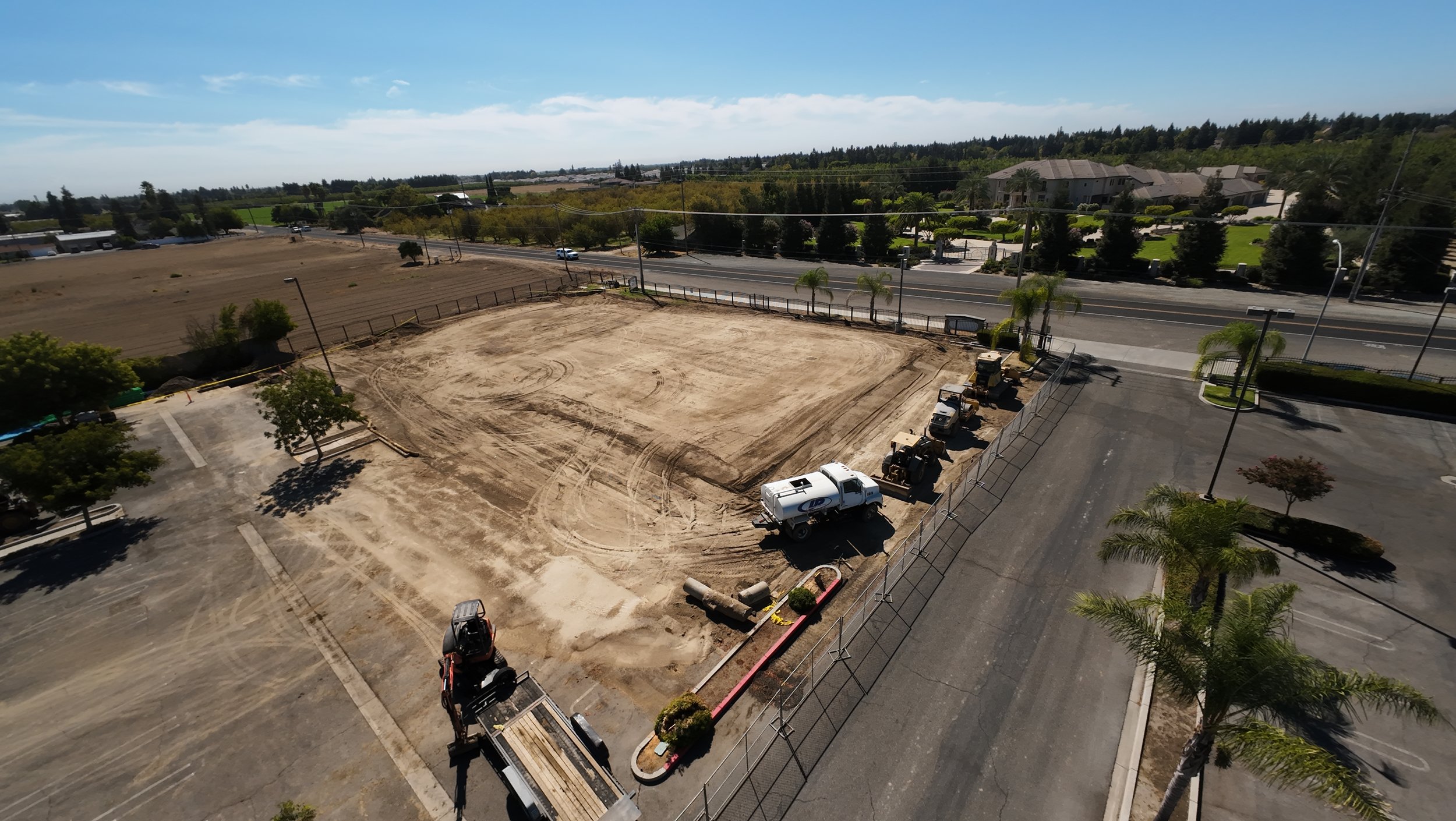 High aerial of a level graded pad with adjacent fields, road, and staging in Denair, California